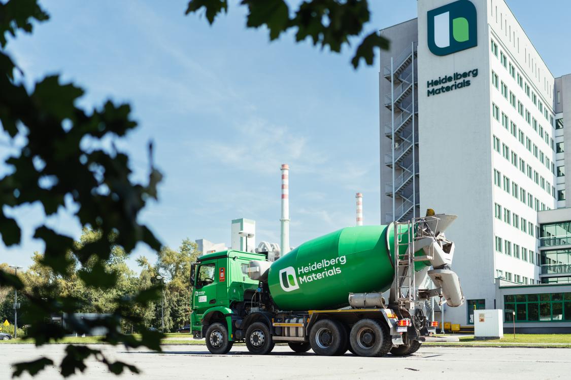 Green ready-mixed concrete truck in front of a multistorey building with the inscription ‘Heidelberg Materials’